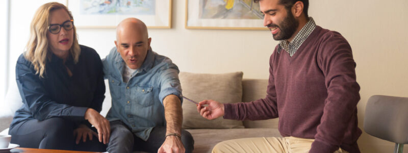 Middle aged couple discussing renovation project with designer and choosing new wall colors. Men and woman sitting in living room at home and talking. Interior design concept
