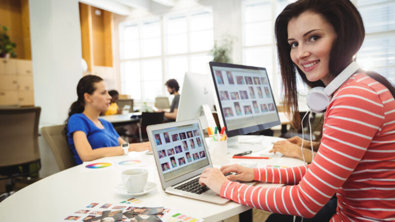 Graphic designer looking at camera while colleague working in background in the office